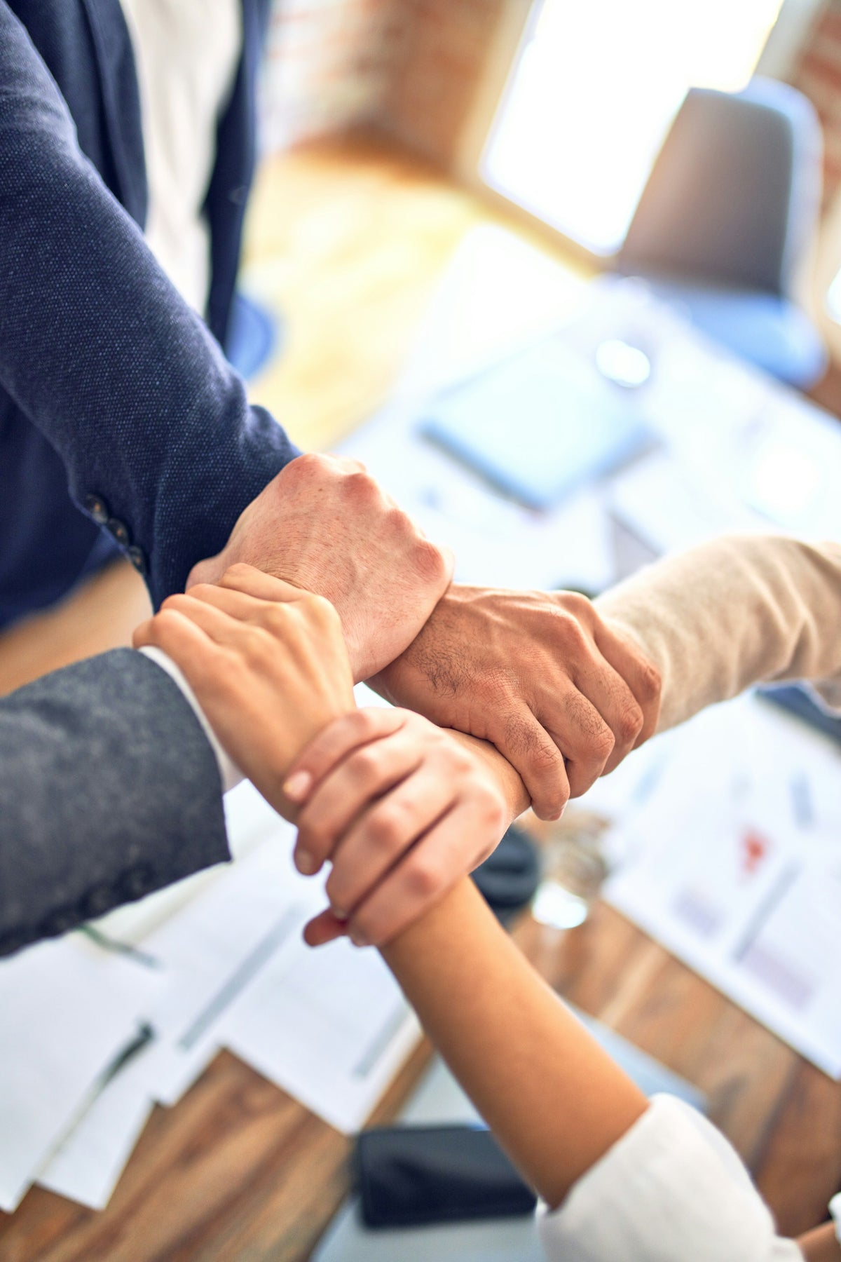 互いの手首をつなぎ協力する企業チーム